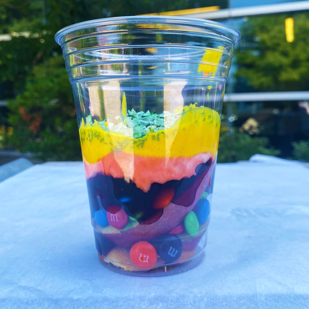 Dino parfait with many colored layers sitting inside a clear plastic cup.